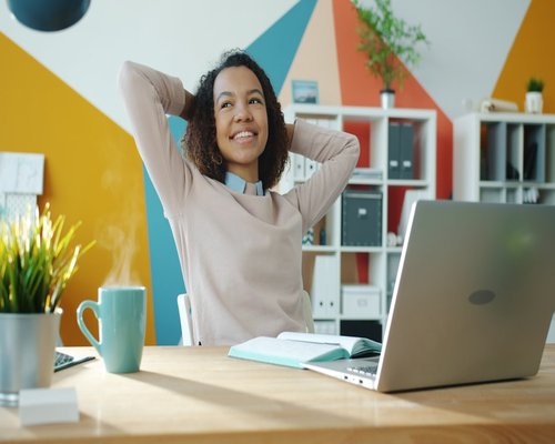 Woman stretching arms and looking away from laptop at her desk